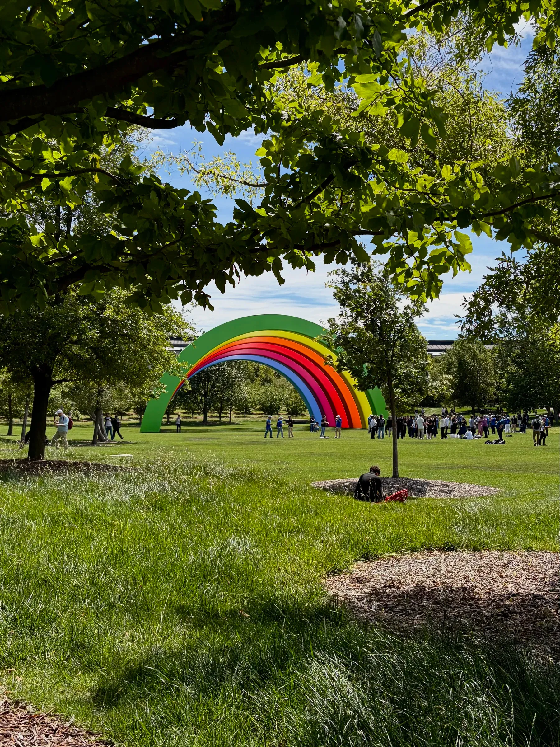 Rainbow-colored arch on the Apple Park meadow with the Ring building visible through the trees