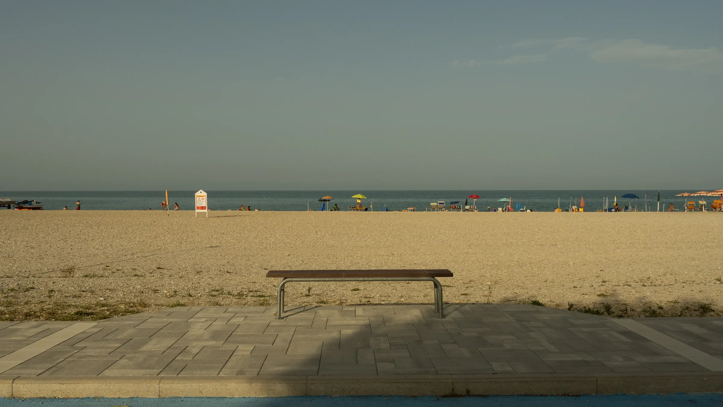 Solitary wooden bench on a paved walkway overlooking the Adriatic at Marina Palmense