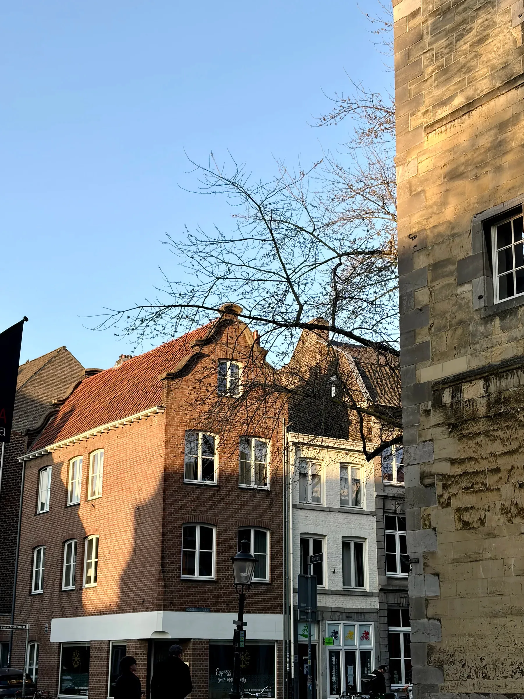 Narrow Maastricht shopping street leading toward a church tower at dusk