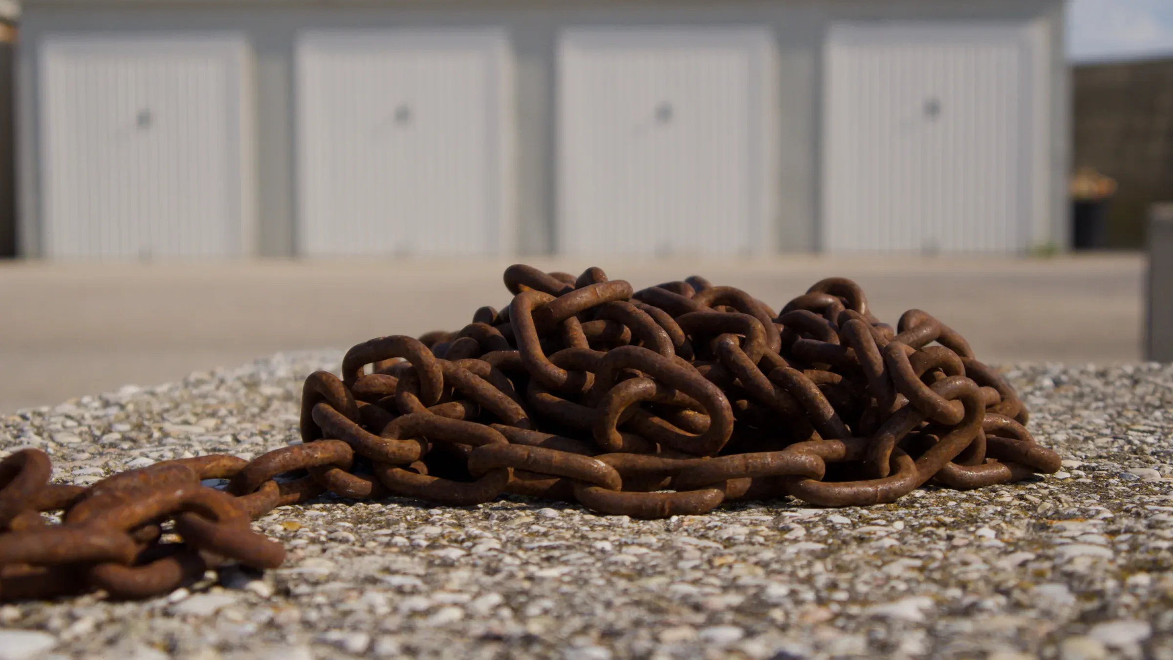 Heavy rusted mooring chains piled on concrete in front of white marina storage garages