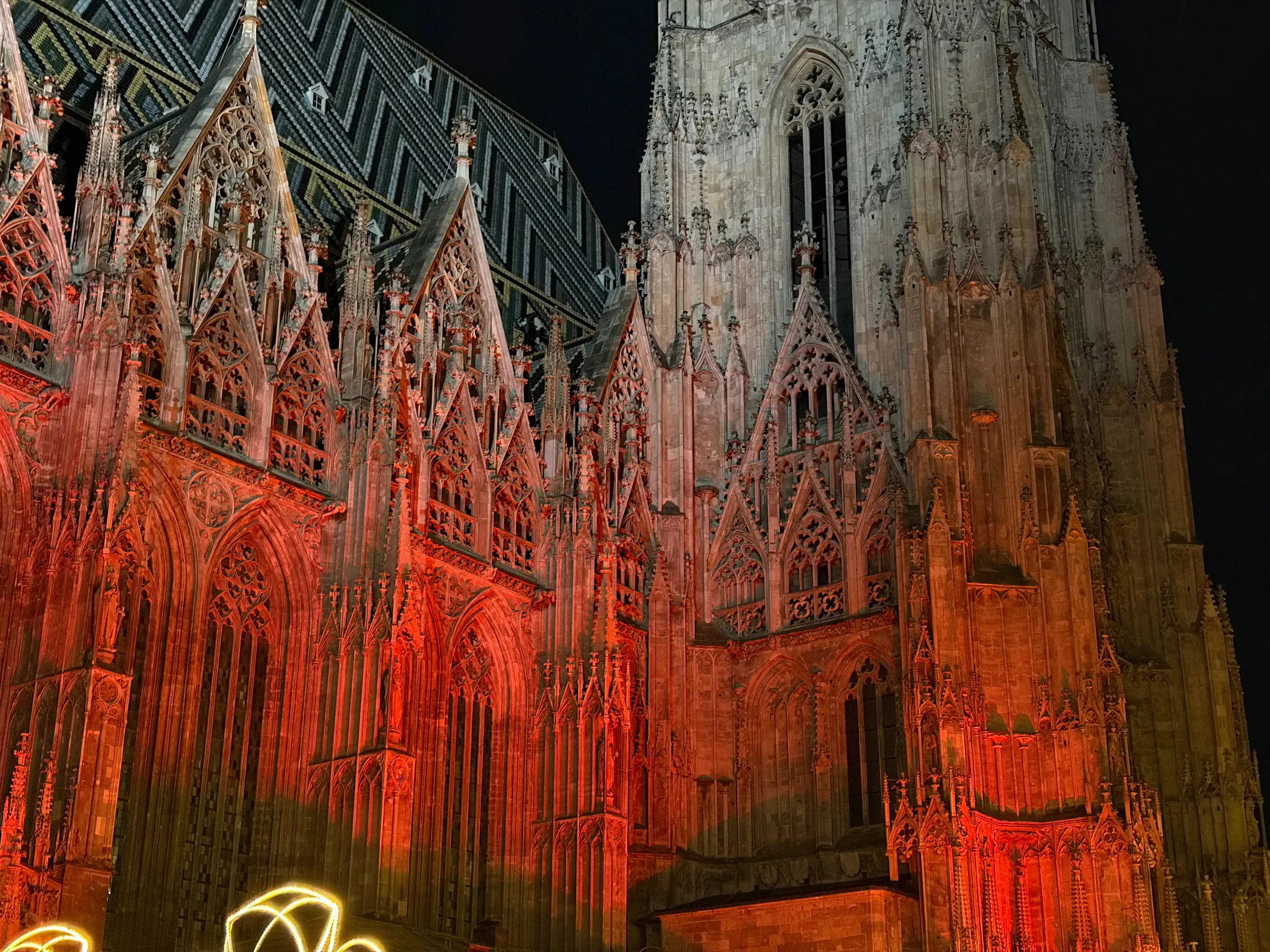 Red-lit Gothic facade and patterned roof tiles of Stephansdom at night